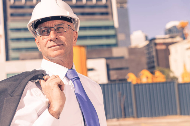 Engenheiro de construção confiante em hardhat e com jaqueta no ombro
 - Foto, Imagem