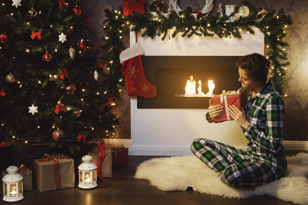 Happy woman with a Christmas gift sitting beside the fire place - Photo, Image