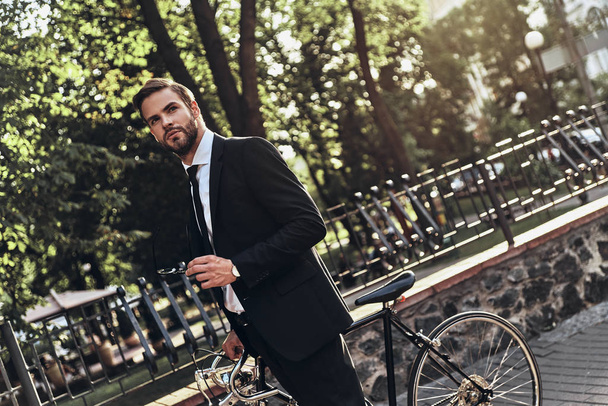 Un uomo d'affari premuroso che guarda altrove mentre cammina all'aperto con la bicicletta
  - Foto, immagini