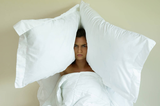 Woman with pillows on her head because she don't wanna hear noise - Foto, afbeelding