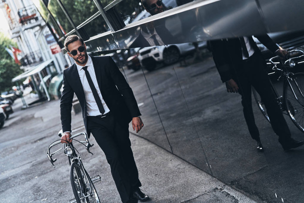 handsome businessman pulling bicycle while walking outdoors - Photo, Image