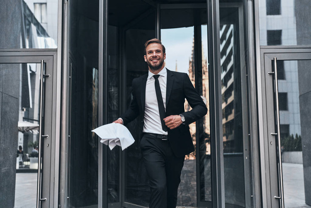 successful businessman holding document while walking outdoors from office building            - Foto, afbeelding