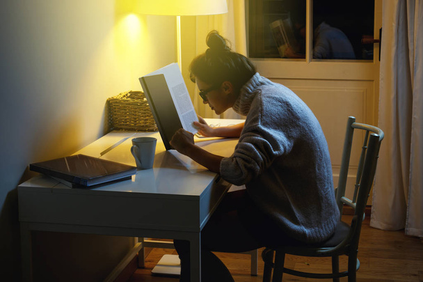 Woman wearing a warm woolen sweater is reading book at middle of the night - 写真・画像