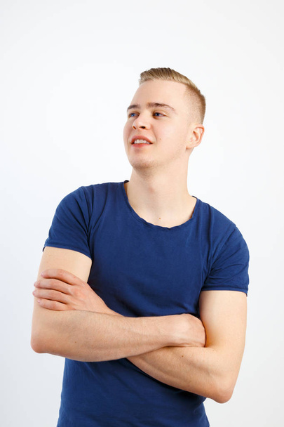 Jovem homem bonito feliz em camisa azul e jeans posa com braços cruzados no estúdio branco
 - Foto, Imagem