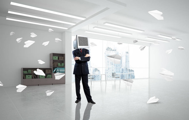 Businessman in suit with monitor instead of head keeping arms crossed while standing among flying paper planes inside office building. 3D rendering. - Foto, Bild