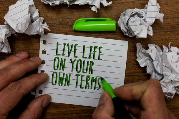 Word writing text Live Life On Your Own Terms. Business concept for Give yourself guidelines for a good living Hand hold green pen and words on white page paper lobs around on wooden desk - Photo, Image