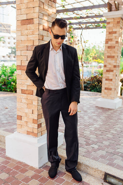 Young stylish handsome man posing in modern city park, wearing suit and sunglasses. - Foto, Imagem