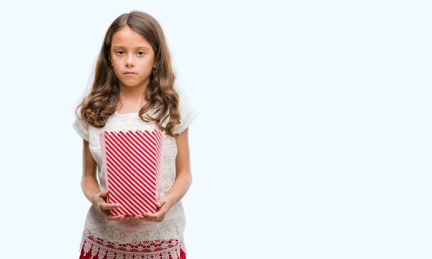 brünettes hispanisches Mädchen, das Popcorn mit selbstbewusstem Gesichtsausdruck isst und ernsthaft denkt - Foto, Bild