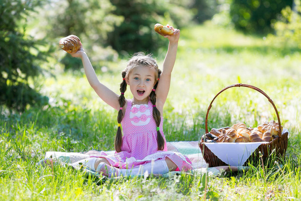 Дівчина сидить на траві, піднімаючи руки хлібом угору. Дитина тримає в руках хліб
. - Фото, зображення