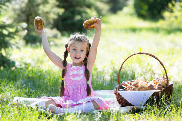 A girl sits on the grass raising her hands with bread high up. The child holds bread in his hands. - Foto, afbeelding
