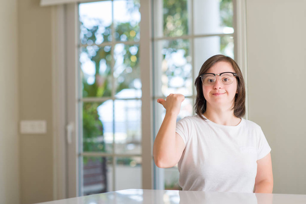 Синдром Дауна женщина дома указывая и показывая с большим пальцем вверх в сторону со счастливым лицом улыбаясь
 - Фото, изображение