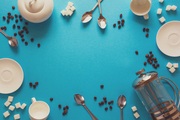 Various coffee making accessories: French coffee press, cups, saucers, coffee beans, spoons and sugar on blue paper background. Good morning concept. Space for copy. Top view. Flat lay. Toned - Фото, зображення