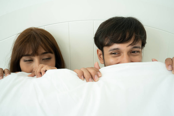 Пара влюбленных на кровати, прячущихся под одеялом и глядящих друг на друга, чувствующих себя счастливыми
 - Фото, изображение