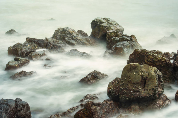 Μακροχρόνια έκθεση Θαλασσογραφία με αφρισμένα κύματα εκτοξεύεται ενάντια σε μια βραχώδη ακτή της Ταϊλάνδης το πρωί ώρα - Φωτογραφία, εικόνα