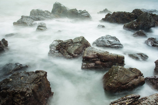 Довгий морський пейзаж з пінистими хвилями, що стискаються на скелястому березі Таїланду в ранковий час
 - Фото, зображення