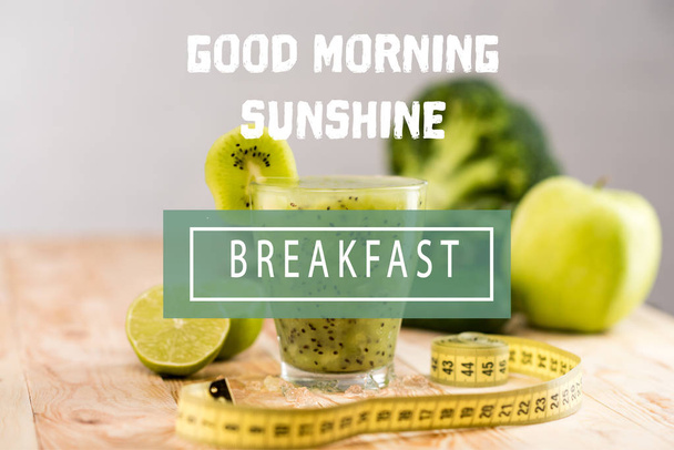 vers fruit smoothie in glas stuk van kiwi's, limoenen en meetlint op tafel komen, met "good morning sunshine" en "ontbijt" belettering - Foto, afbeelding