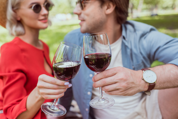 happy couple clinking with glasses of red wine in park - Foto, imagen