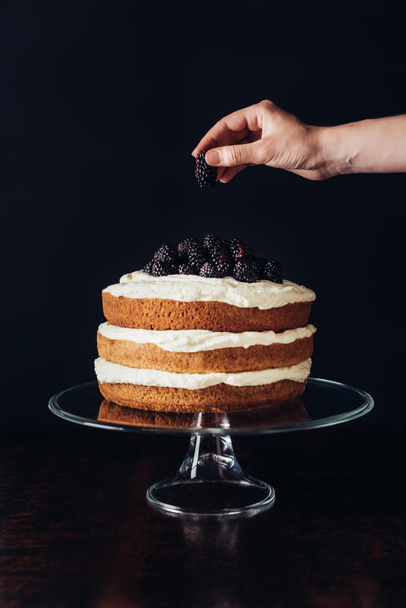 plan recadré de femme décoration savoureux gâteau mûre sur support en verre sur noir
 - Photo, image