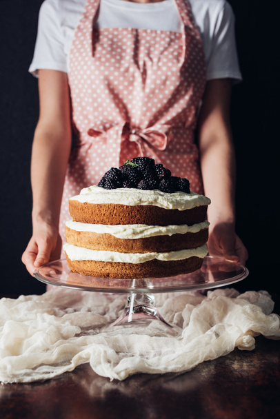cropped shot of woman holding freshly baked blackberry cake on glass stand on black - Fotoğraf, Görsel