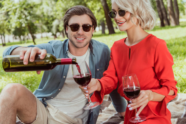 boyfriend pouring red wine in glasses in park - Fotó, kép