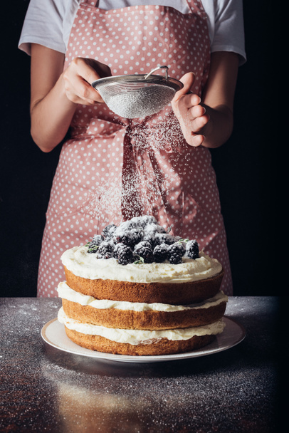 cropped shot of woman spilling sugar powder onto tasty blackberry on black - Valokuva, kuva