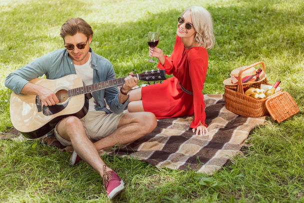 ハンサムな彼氏のピクニック ガール フレンドのためのアコースティック ギターを演奏 - 写真・画像