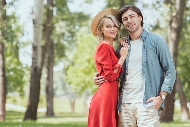 smiling girlfriend and boyfriend hugging in park and looking at camera - Foto, imagen