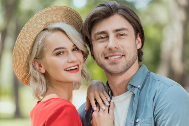 portrait of smiling girlfriend and boyfriend hugging in park and looking at camera  - Foto, imagen