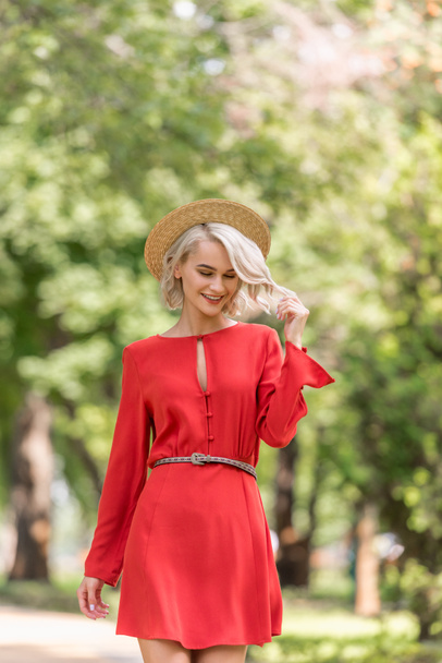 mosolygó gyönyörű lány piros ruhában és szalmakalap park séta  - Fotó, kép