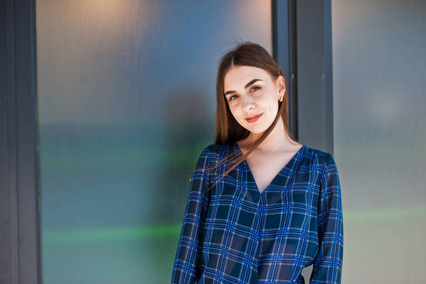 Portrait of young brunette girl in blue checkered shirt against large windows. - Foto, afbeelding