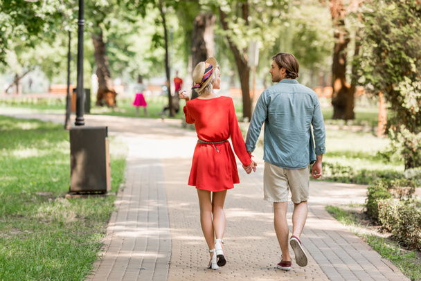 back view of girlfriend and boyfriend walking together in park and looking at each other - Photo, Image
