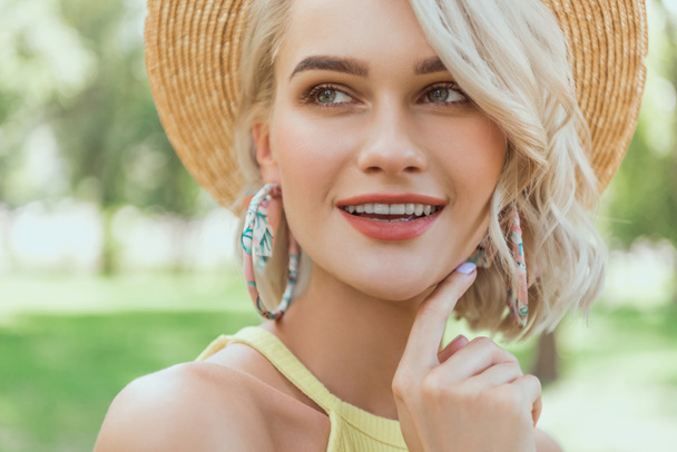 portrait of attractive blonde girl in straw hat looking away in park - Photo, Image