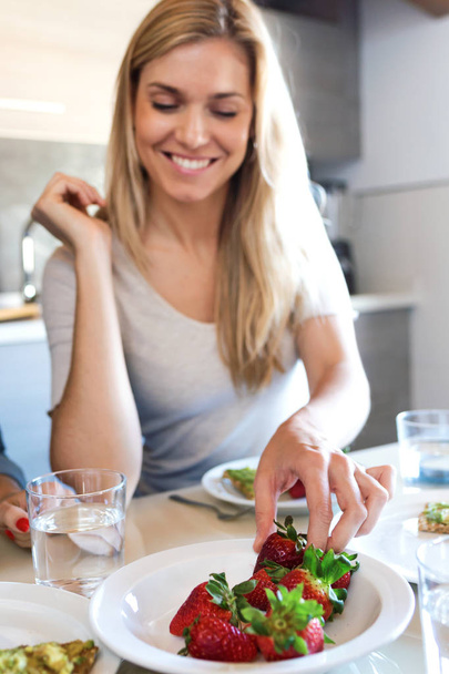 Shot of beautiful young woman eating strawberries at home. - Фото, изображение
