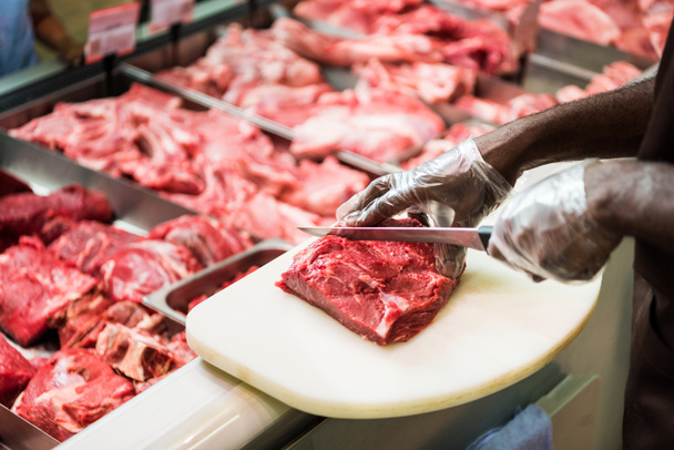 részleges kilátás nyílik afroamerikai férfi elárusítónő vágás steak a nyers hús szupermarketben  - Fotó, kép