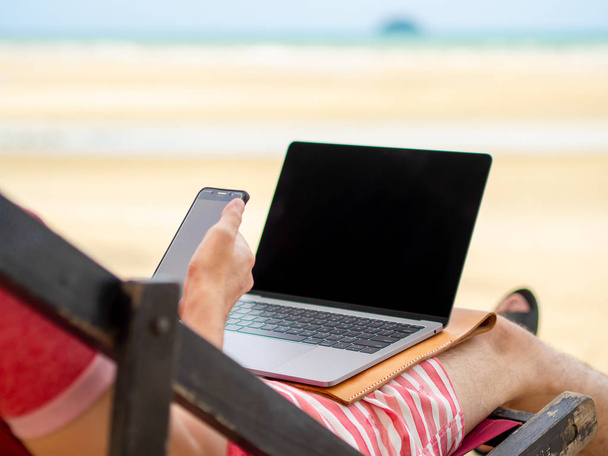 Hombre relajarse en la cama del campamento y trabajar en línea mientras está de vacaciones en la playa en Tailandia
. - Foto, imagen