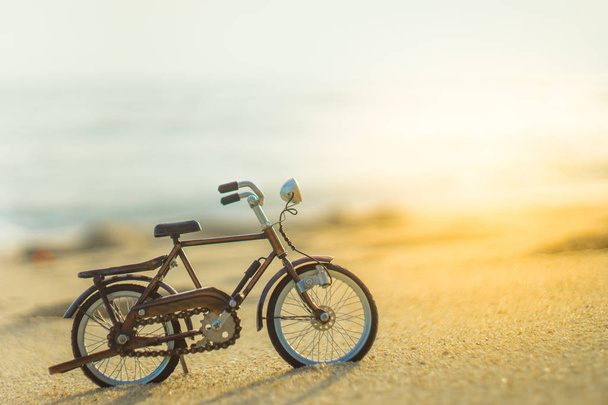 велосипедний транспорт іграшка на піщаному морському пляжі ввечері небо заходу сонця, з жовтим світловим променем
 - Фото, зображення