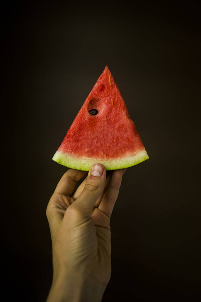 Slice of watermelon in hand. Against a dark background - Foto, Imagem