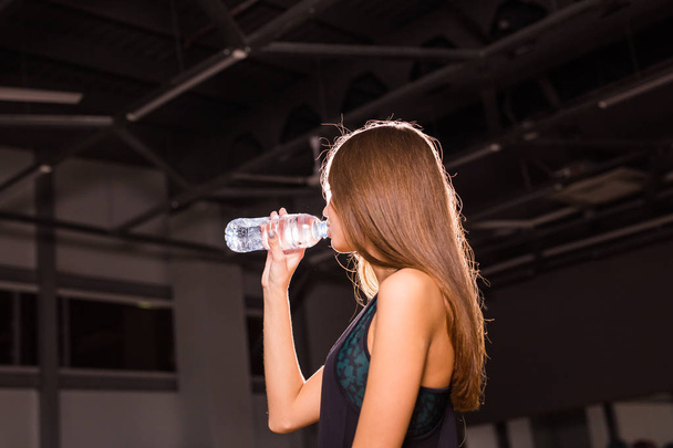 Fitness nainen juo vettä pullosta. Lihaksikas nuori nainen kuntosalilla tauolla harjoituksesta
. - Valokuva, kuva
