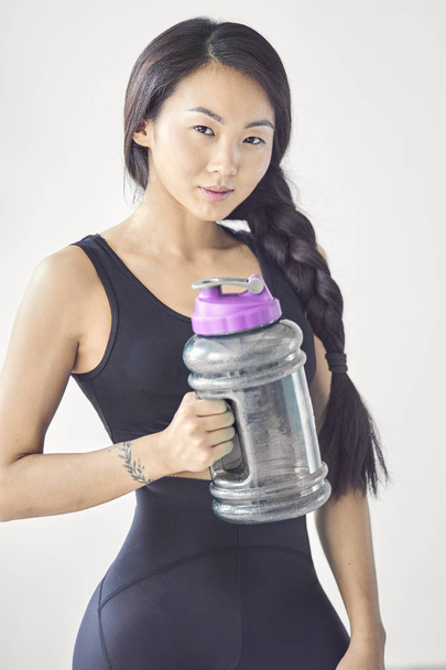 アジアの女の子は、白い背景の上の飲料水のボトルを保持します。フィットネスの概念、医療 - 写真・画像