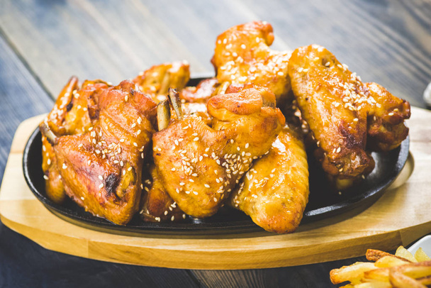 жареные куриные крылышки с кунжутом на чугунной тарелке - Фото, изображение