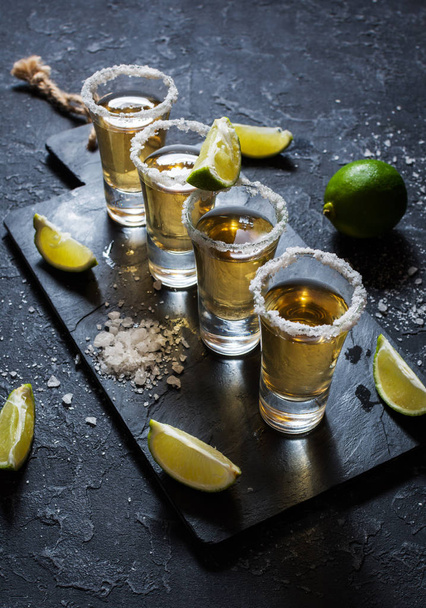 mexikanischer Gold-Tequila mit Limette und Salz auf schwarzem Steinhintergrund - Foto, Bild