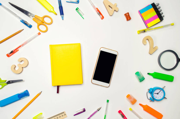 mobile phone and yellow notebook in the desk. white background. concept of education. back to school. creative mess on the desktop. desk. stationery. smartphone. place for text. flat lay. - Photo, Image
