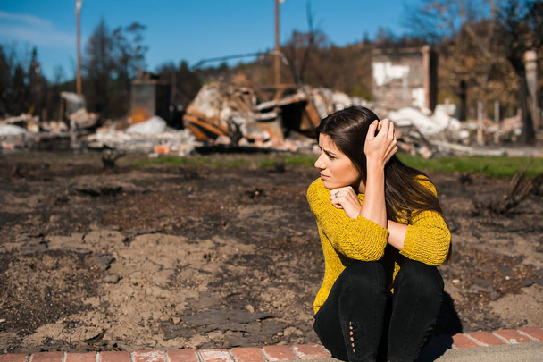 Грустная женщина-домовладелец держит голову за руку, проверяя сгоревший дом и двор после пожара, последствия несчастного случая. Руины после пожара, потерь и отчаяния
. - Фото, изображение