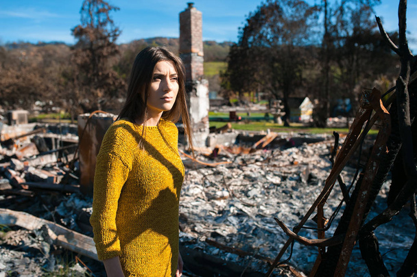 Young owner woman checking burned and ruined house and yard after fire, consequences of fire disaster accident. Ruins after fire disaster, loss and despair concept. - Photo, Image
