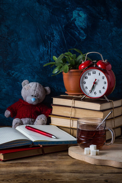 geöffnetes Tagebuch, Tasse heißen Tee, Bücher, roter Wecker auf dunkelblauem Hintergrund. Schulkonzept. - Foto, Bild