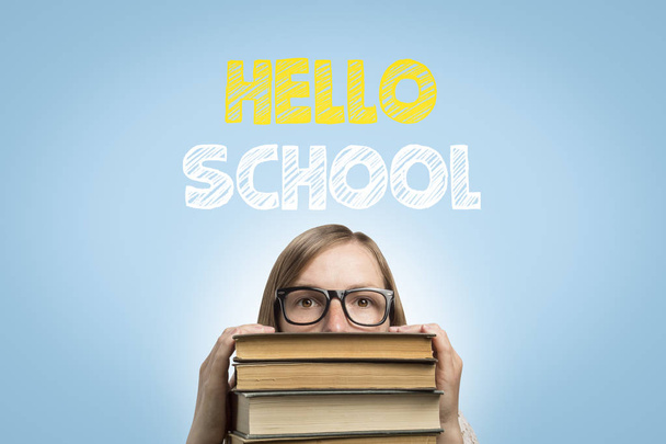Fiatal lány diák szemüveg peeks ki alóla a halom könyvet egy kék háttér, szöveg Hello iskola. Az új tanév kezdete fogalmának. - Fotó, kép