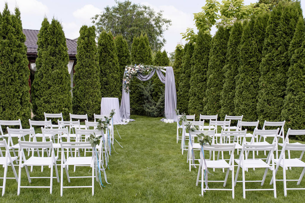 Γαμήλια τελετή σε έναν χορτοτάπητα κάτω από τον ανοικτό ουρανό. Πολλές λευκές καρέκλες και την καμάρα για έναν γάμο - Φωτογραφία, εικόνα