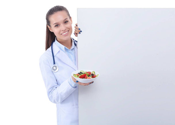 Portrait of a beautiful woman doctor holding a plate with fresh vegetables standing near blank. Woman doctors - Fotoğraf, Görsel