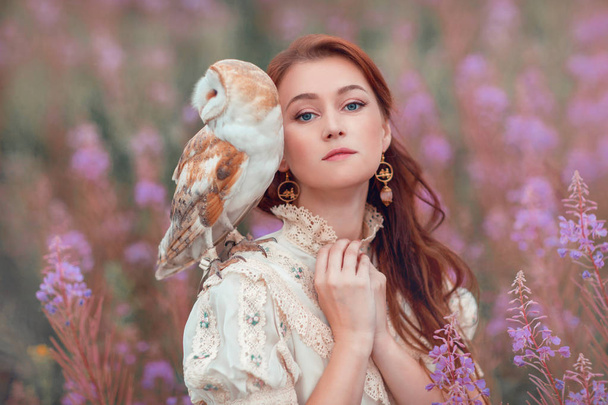 Woman with owl at field of pink flowers. - Фото, изображение