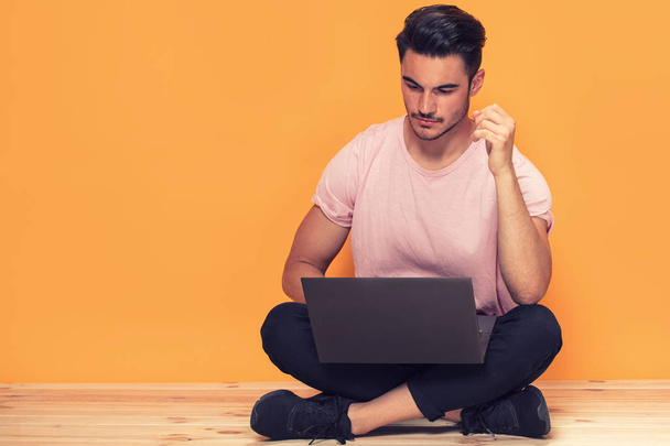 Photo of young handsome man sitting with laptop computer over yellow background. - Foto, Imagem